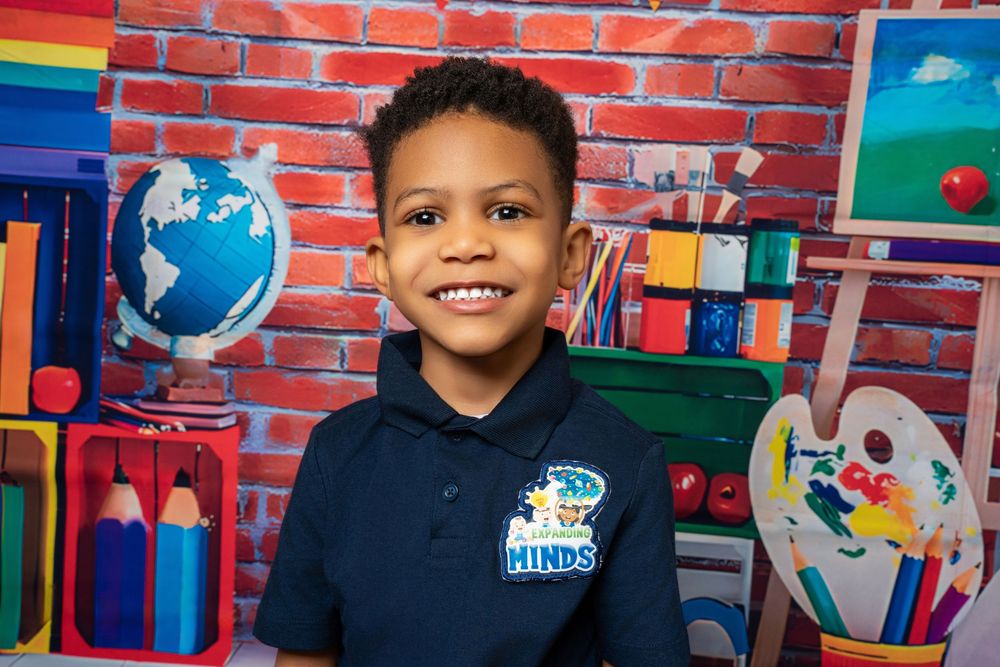 Happy boy in navy Hinds school uniform smiles broadly against colorful classroom brick backdrop.