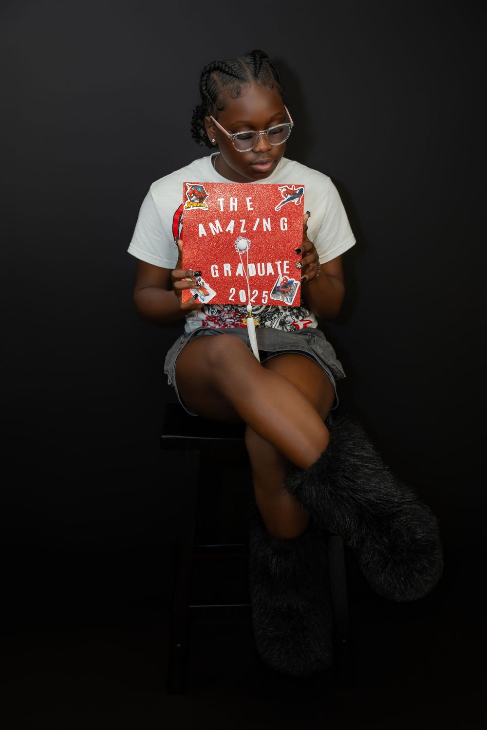 Young graduate sitting against dark background holding red Amazing Graduate 2025 sign.