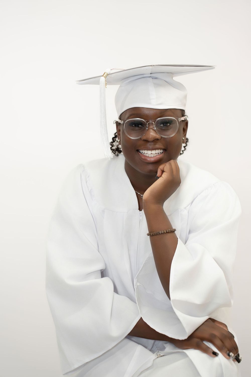 Smiling graduate in white cap and gown posing confidently for senior portrait photo.