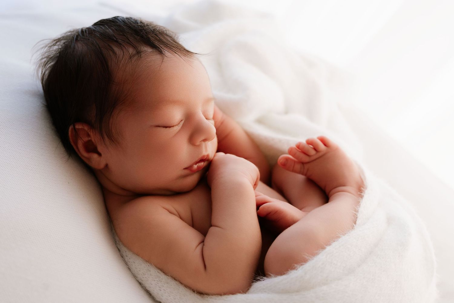 Pregnant woman in white lace dress lying on bed smiling with eyes closed.