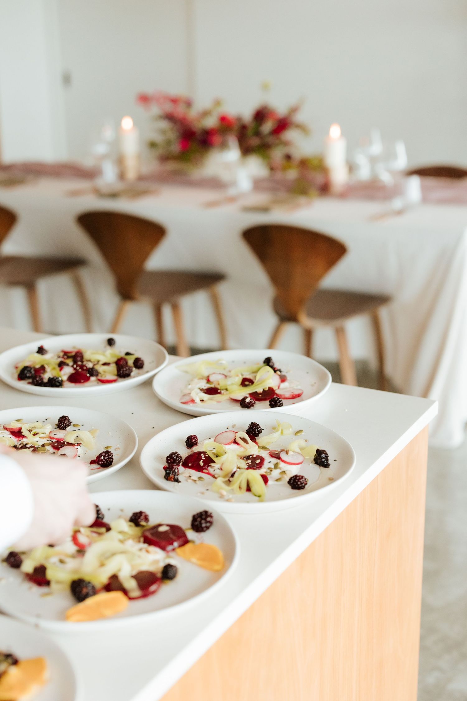 Elegant dinner party setup with plated salads featuring berries and vegetables on a white kitchen counter.