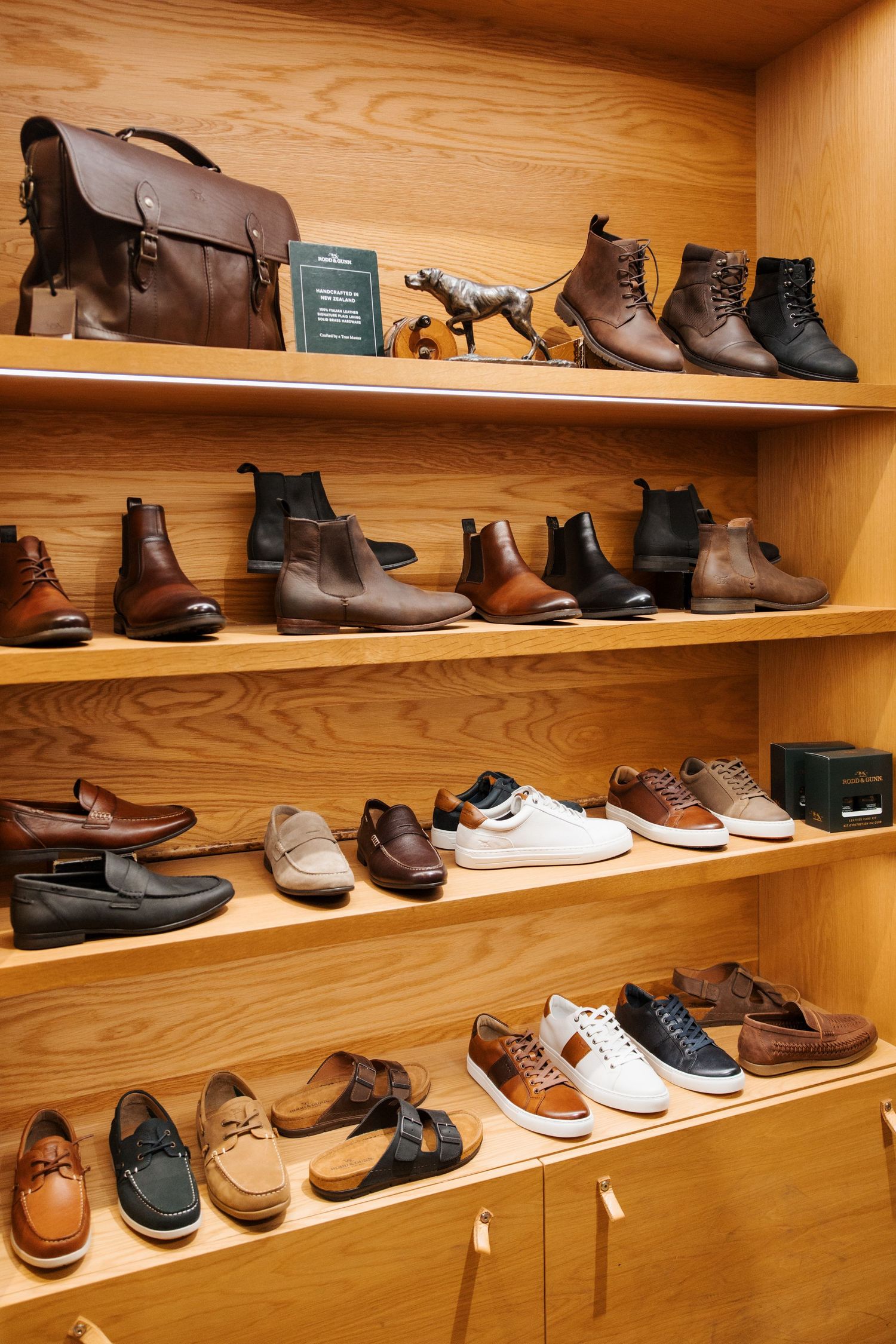 Wooden display shelves showcasing a variety of mens leather shoes, boots, and sneakers in a retail store.
