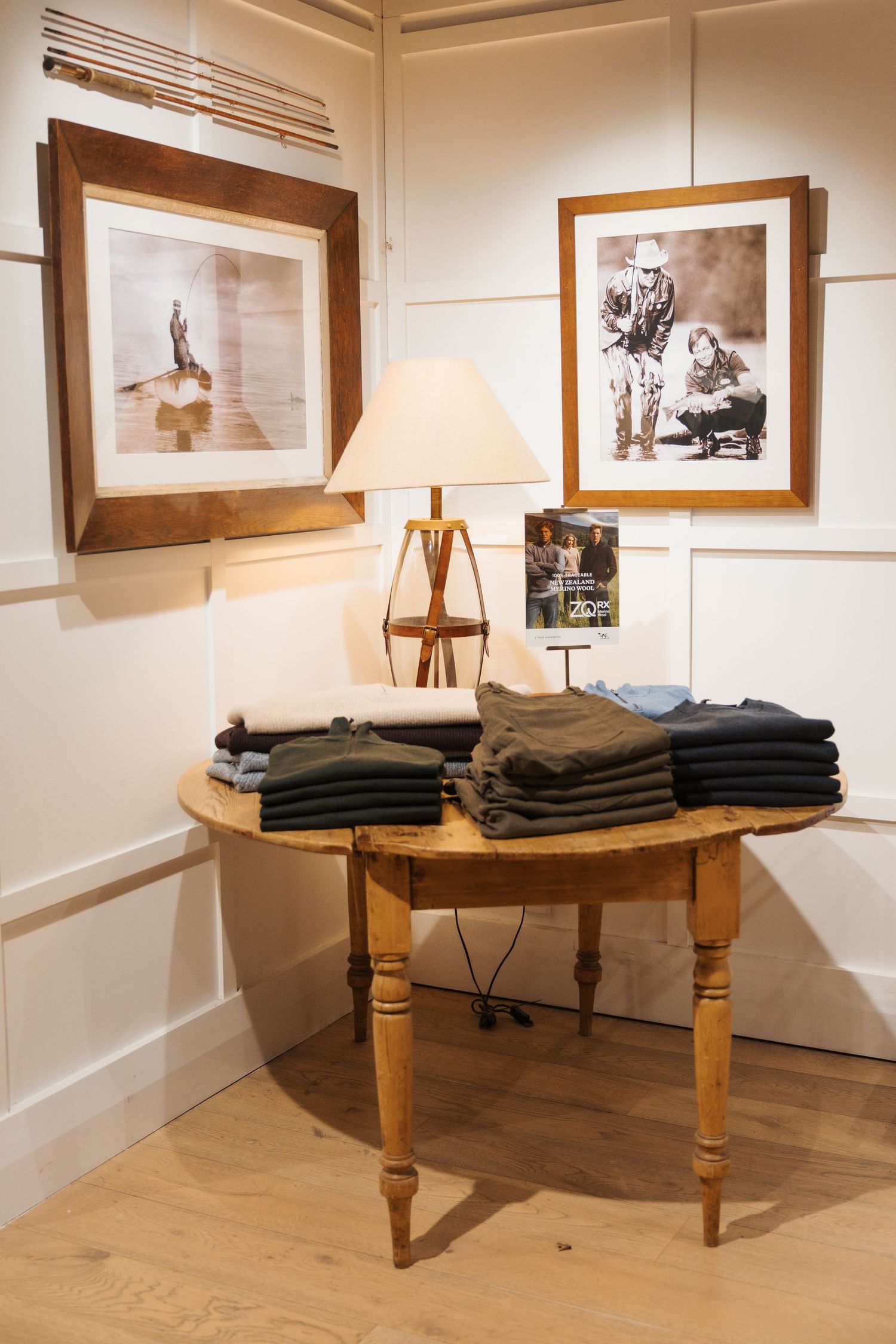 Wooden half-moon table displaying folded clothing stacks beside a lamp, with framed vintage photos on white wainscoting walls.