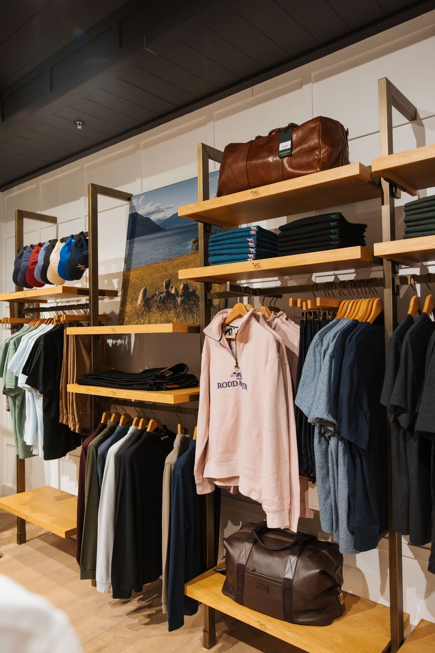Wooden retail clothing display with folded shirts, hanging jackets, hoodies, and leather bags in a modern store.