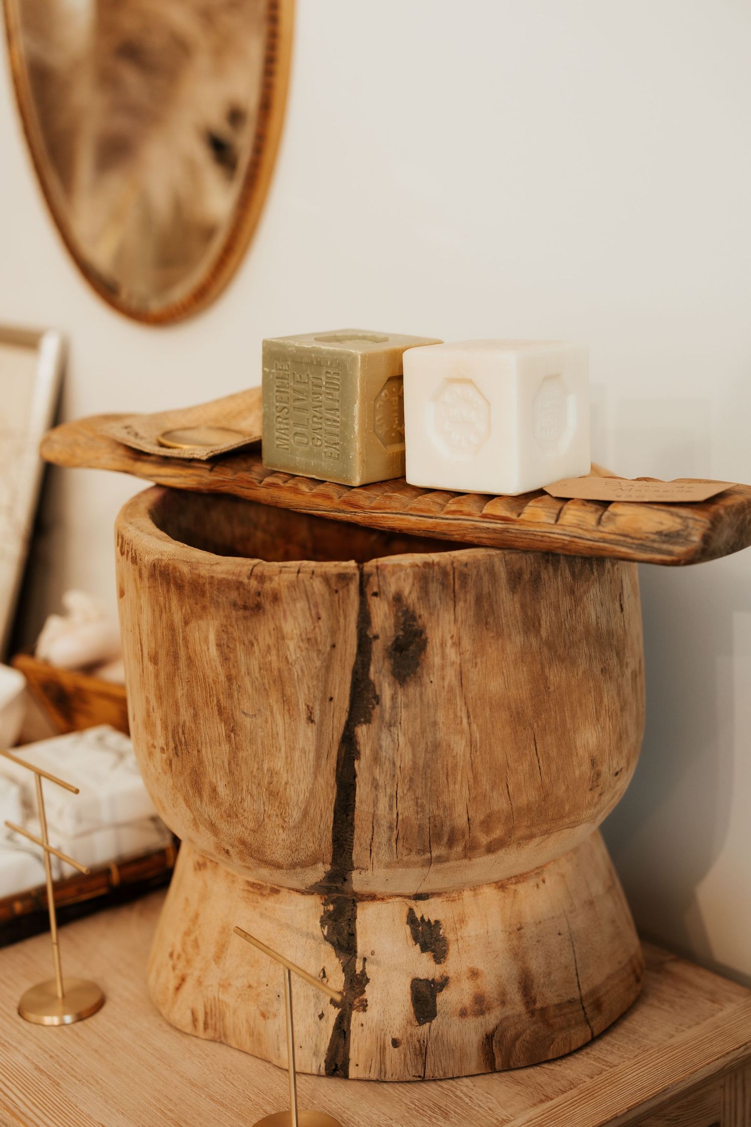 Rustic wooden mortar bowl with two soap bars on a carved tray, displayed on a natural wood side table.