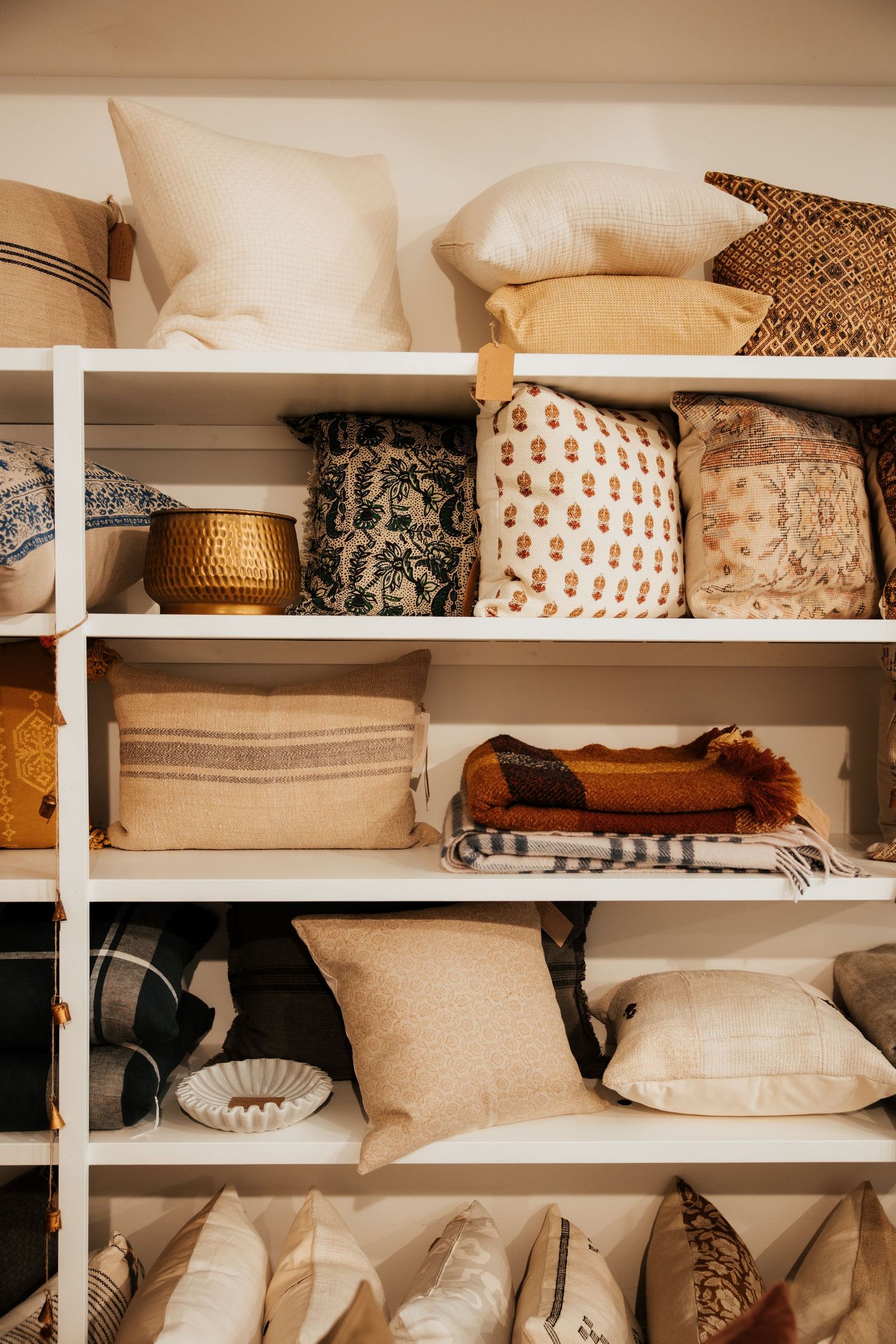 White shelving unit displaying an assortment of decorative throw pillows in neutral tones, patterns, and textures.