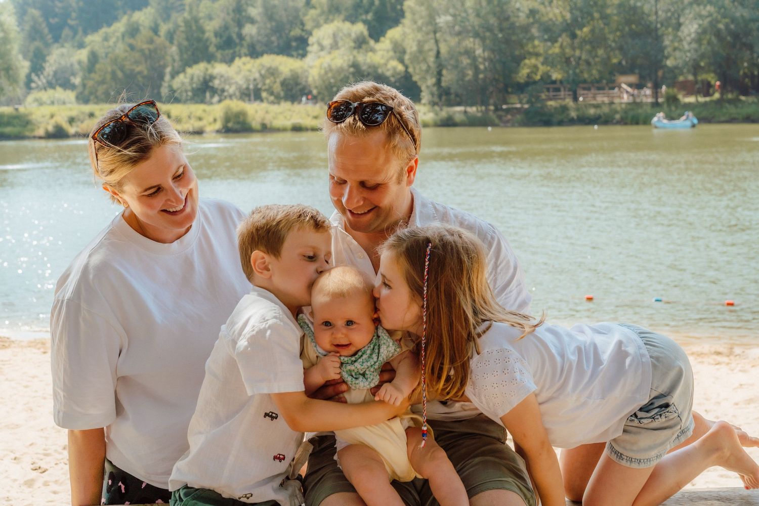 Happy family of five sharing a joyful moment on a sunny beach, parents and children hugging and laughing together.