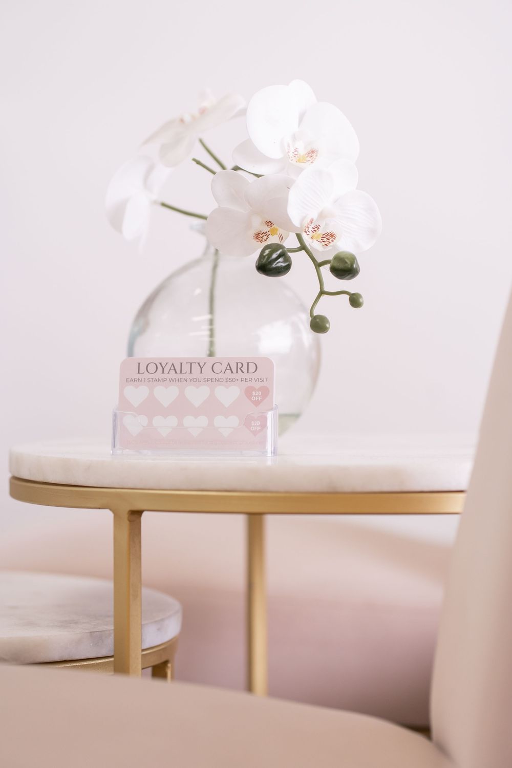 A pink loyalty card displayed beside white orchid flowers in a glass vase on a gold marble side table.
