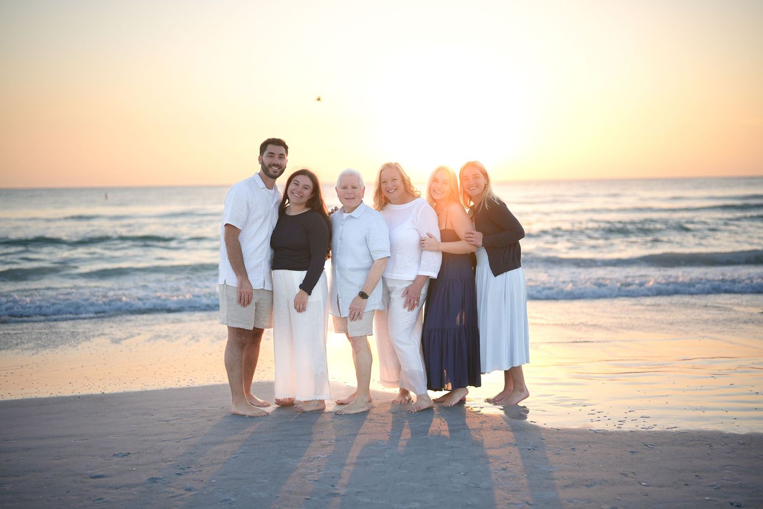 Family group posing together on a sandy beach at golden sunset with ocean waves in the background.