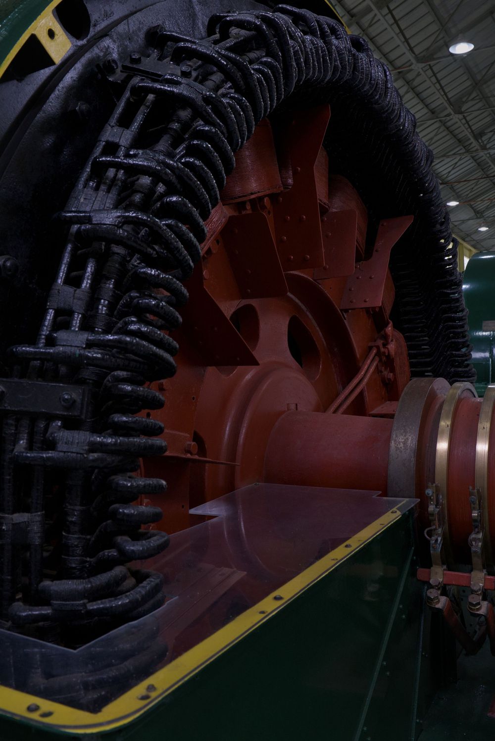 Large red industrial machine rotor with black coil windings displayed in a museum or industrial facility.