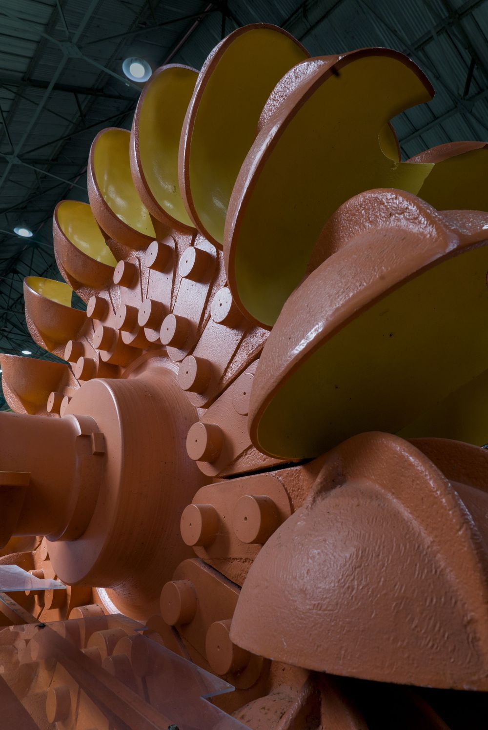 Large industrial turbine rotor with yellow and copper-colored blades displayed inside a warehouse facility.