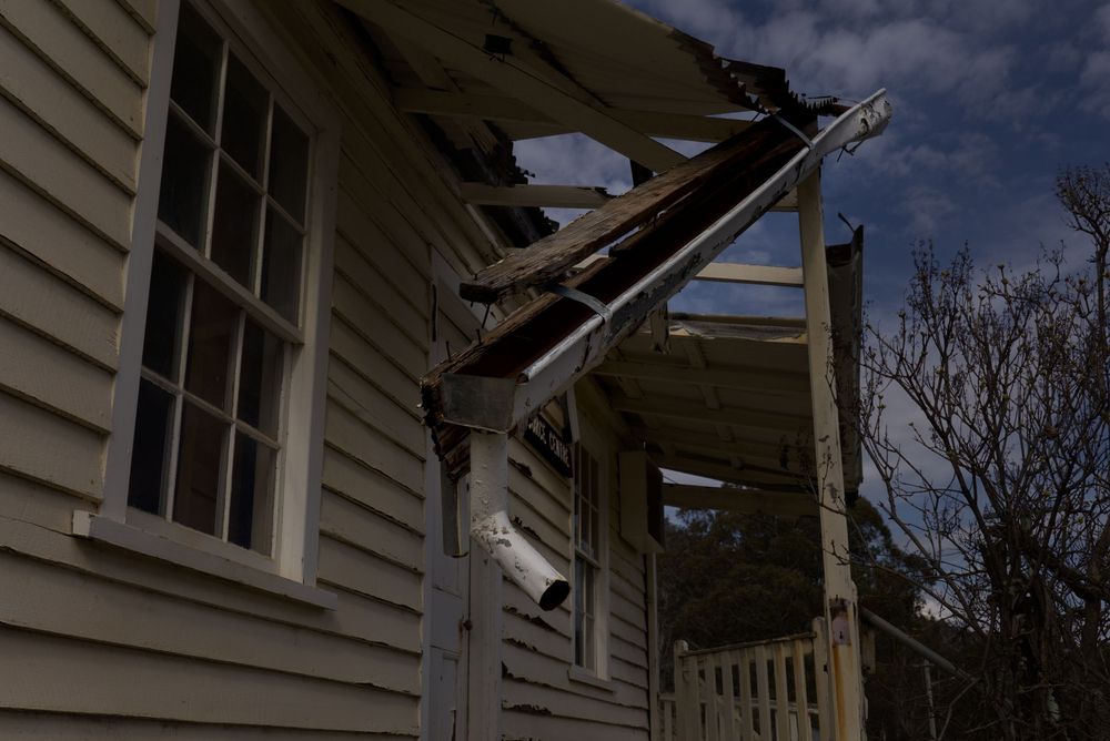 Storm-damaged house with collapsed porch roof and broken wooden beams after severe weather damage.