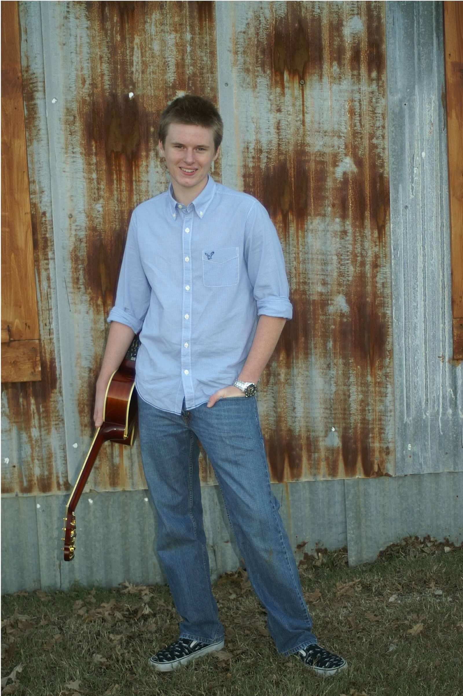 Teen boy poses in front of barn with guitar
