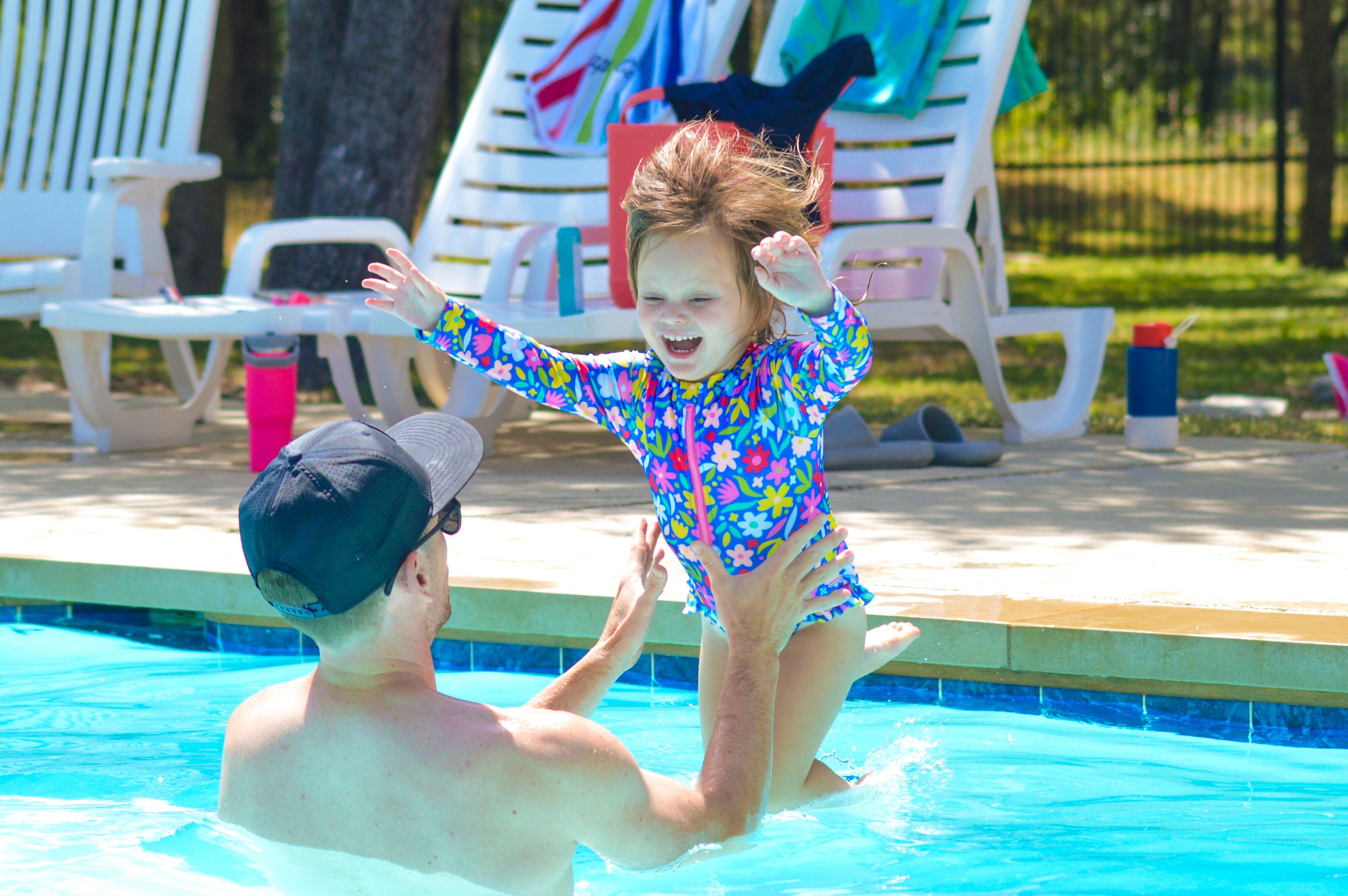 A toddler girl jumps into a pool as her dad catches her