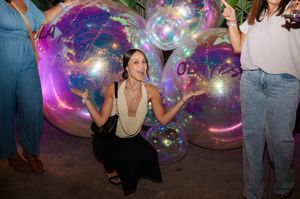 Woman posing with large iridescent decorative bubbles at a colorful nighttime party.