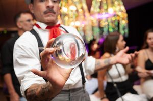 Tattooed performer balancing a crystal ball on his hand at a festive indoor event.