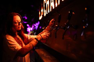 Young woman pouring draft beer at La Canica bar with purple stage lighting.