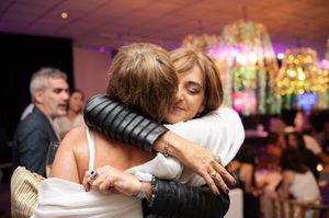Two women sharing a warm embrace at an elegant indoor celebration with colorful lighting.