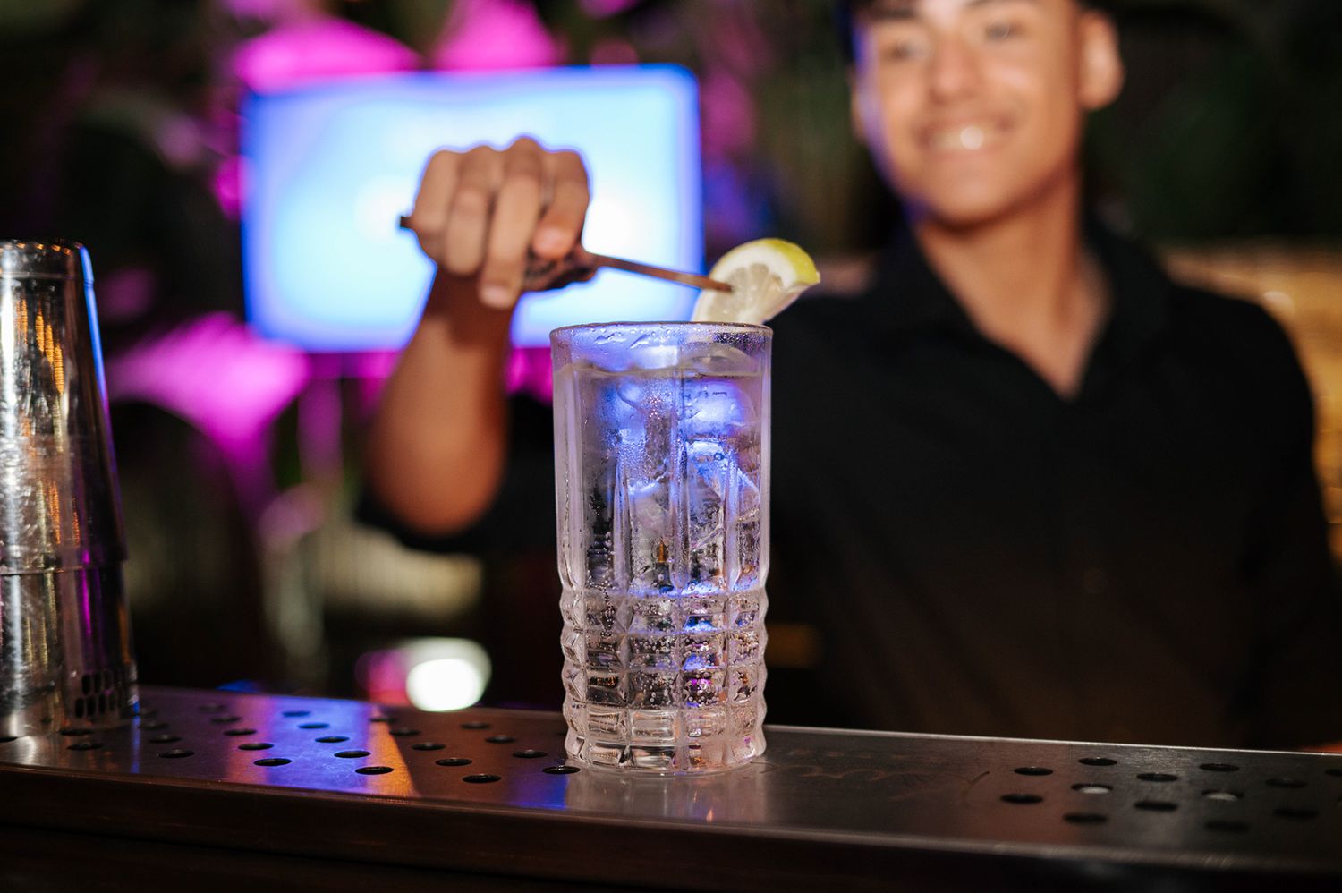 Smiling bartender garnishing a crystal cocktail glass with lime at a nightclub bar.