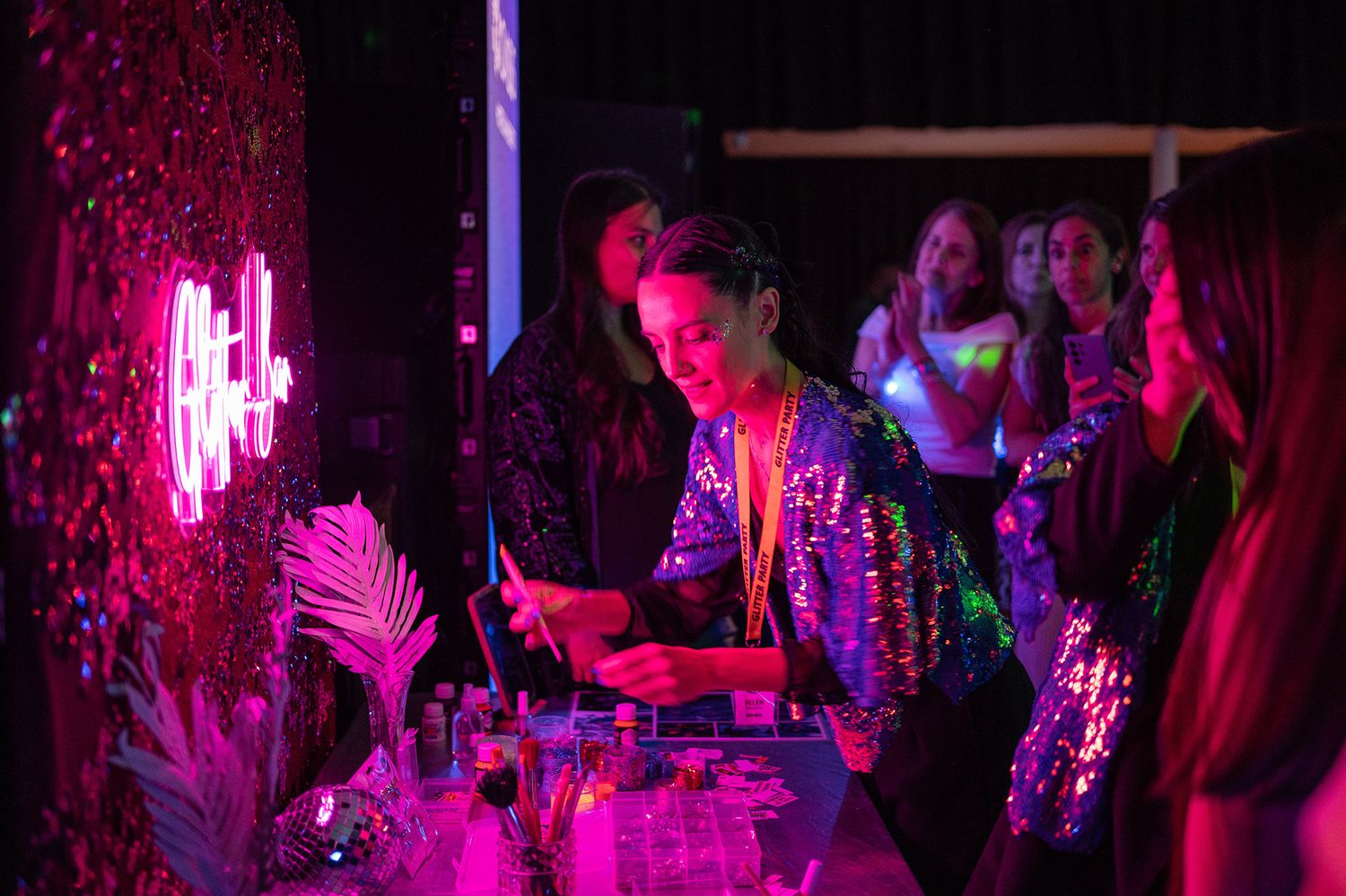 Woman in sequin jacket tending bar under pink neon lights at a glamorous nightclub event.