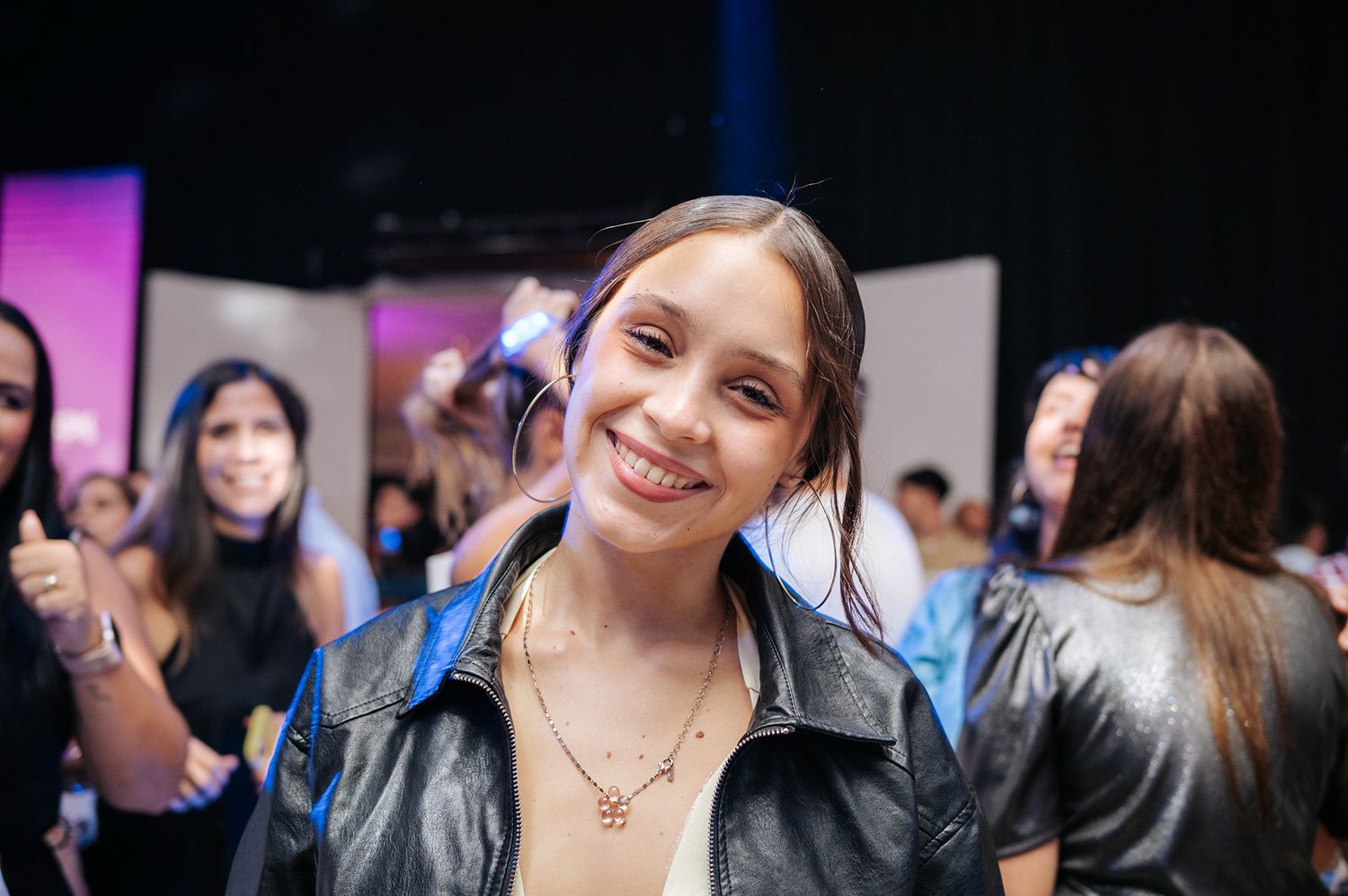 Young woman smiling warmly in a leather jacket at a lively indoor event or party.