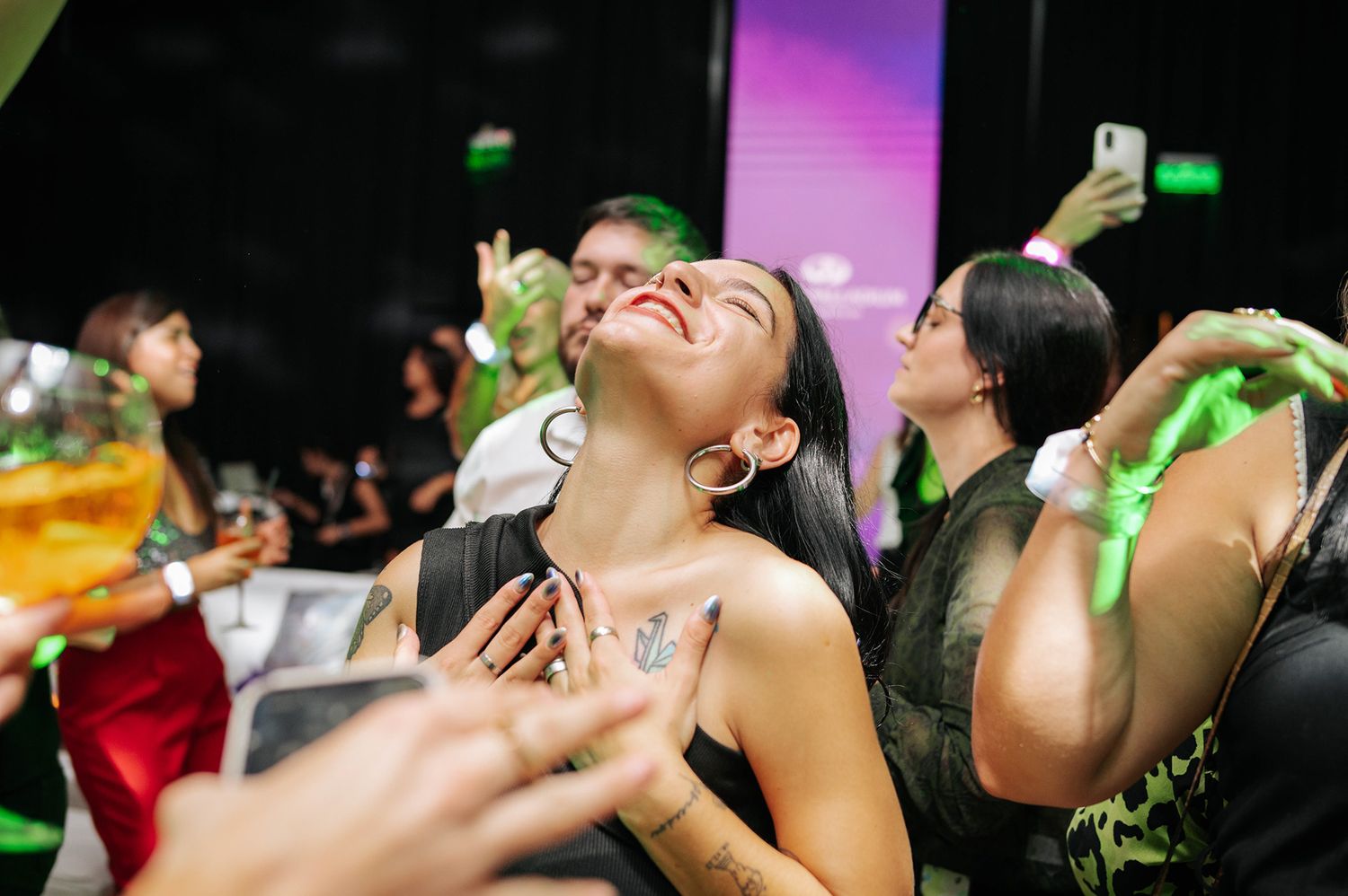 Woman dancing with head tilted back laughing at an energetic nightclub party with green lighting.
