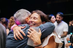 Two people sharing a warm joyful hug and laughing at a social gathering or celebration.
