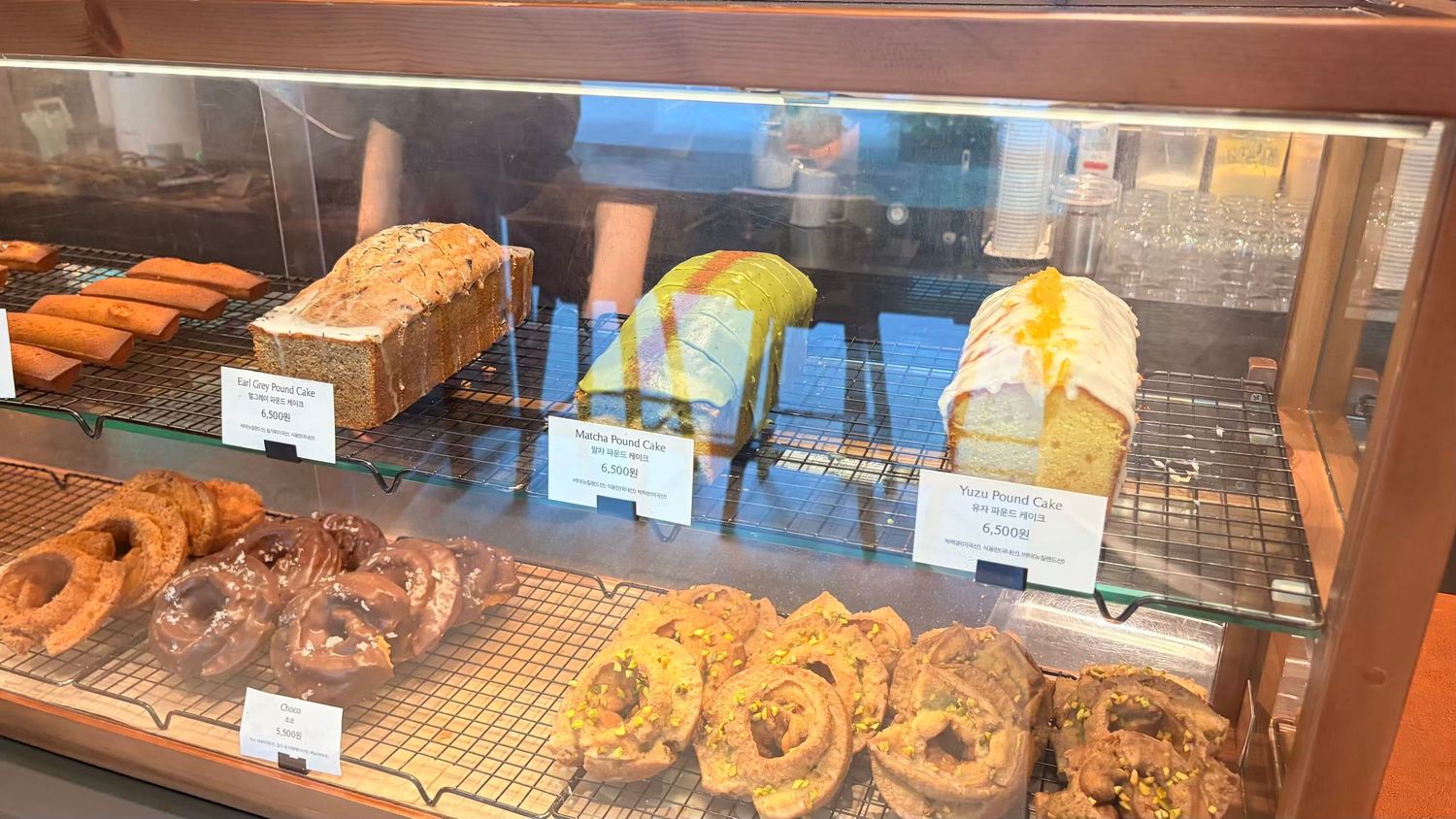 Glass bakery display case filled with fresh donuts, bagels, and sliced loaves of bread with price tags.