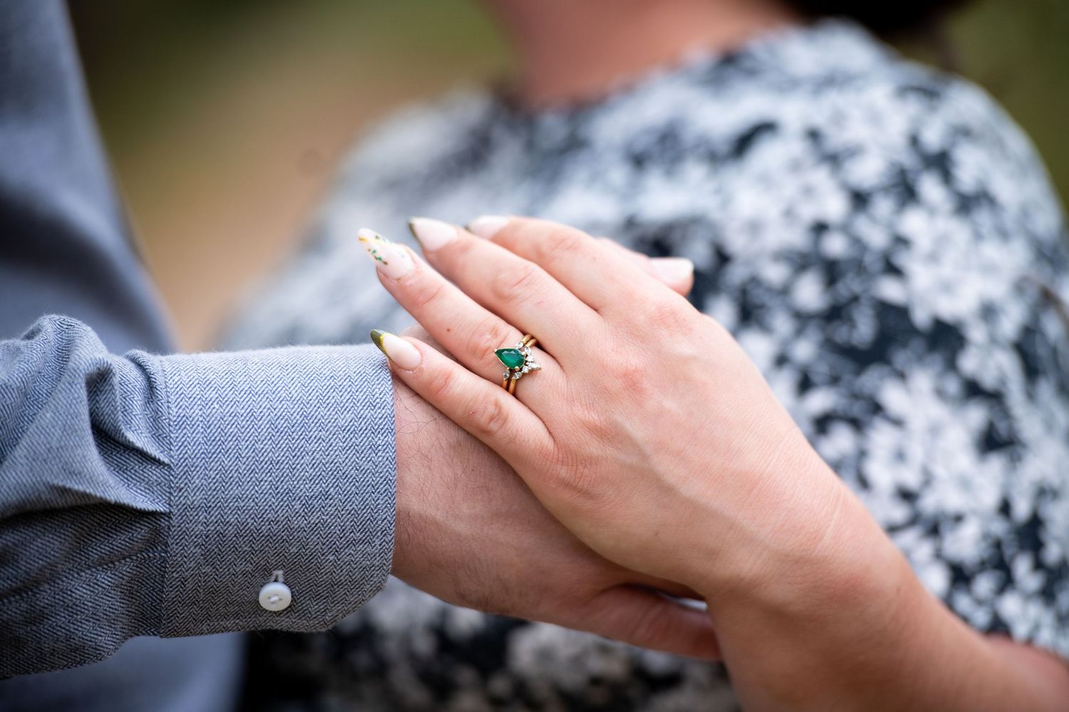 Close-up of a hand wearing a stunning emerald and gold engagement ring resting on a man's wrist.