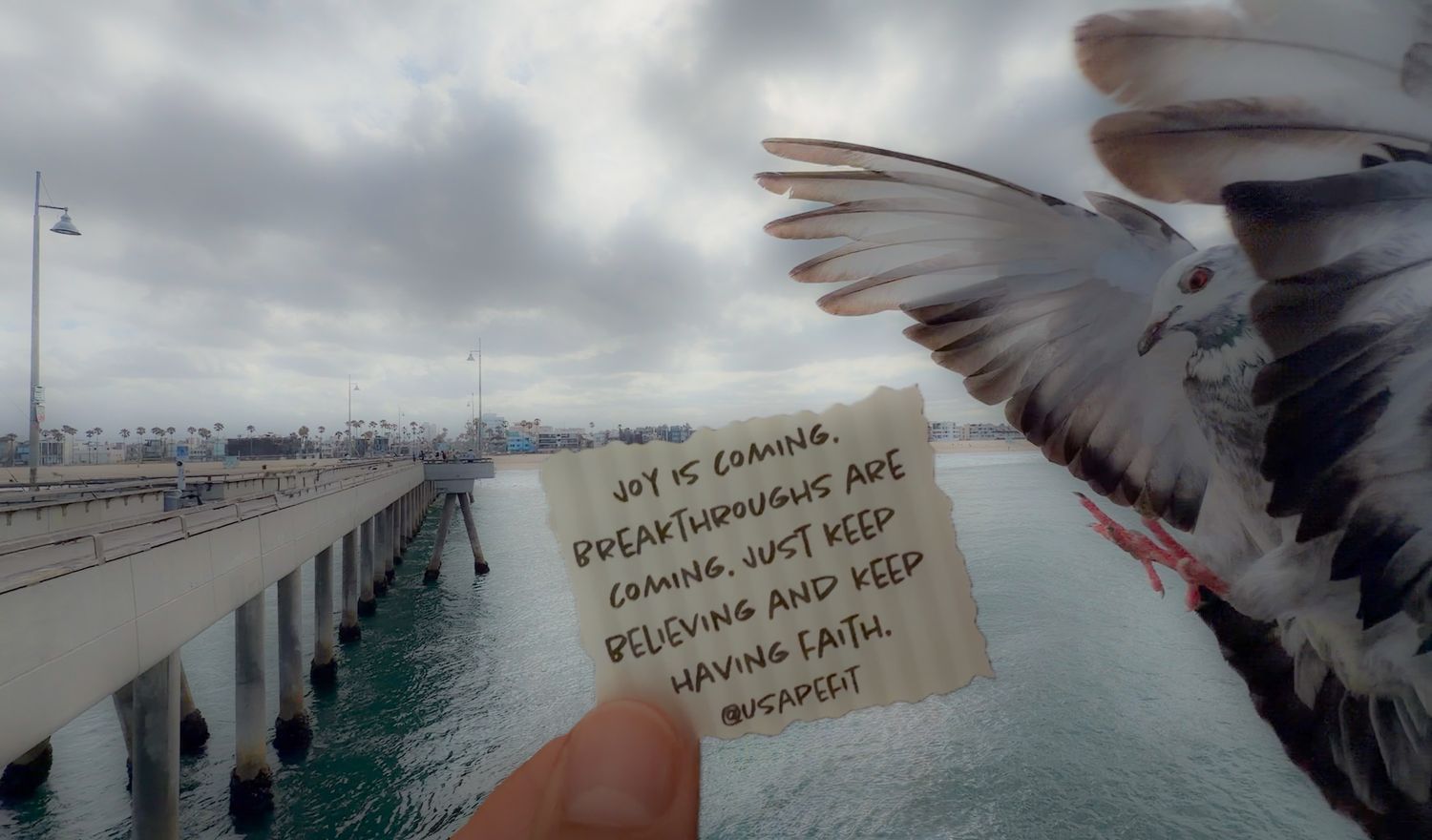 A seagull flies near a pier while a hand holds a note reading inspirational words about joy and breakthroughs coming with faith.