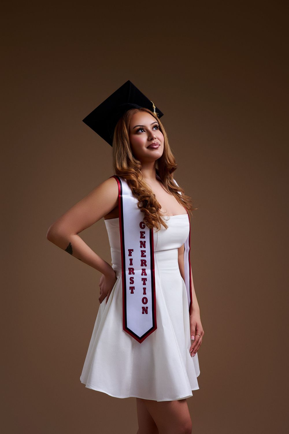 Studio graduation portrait of a first-generation graduate looking up, taken by a North NJ portrait photographer on a brown backdrop.