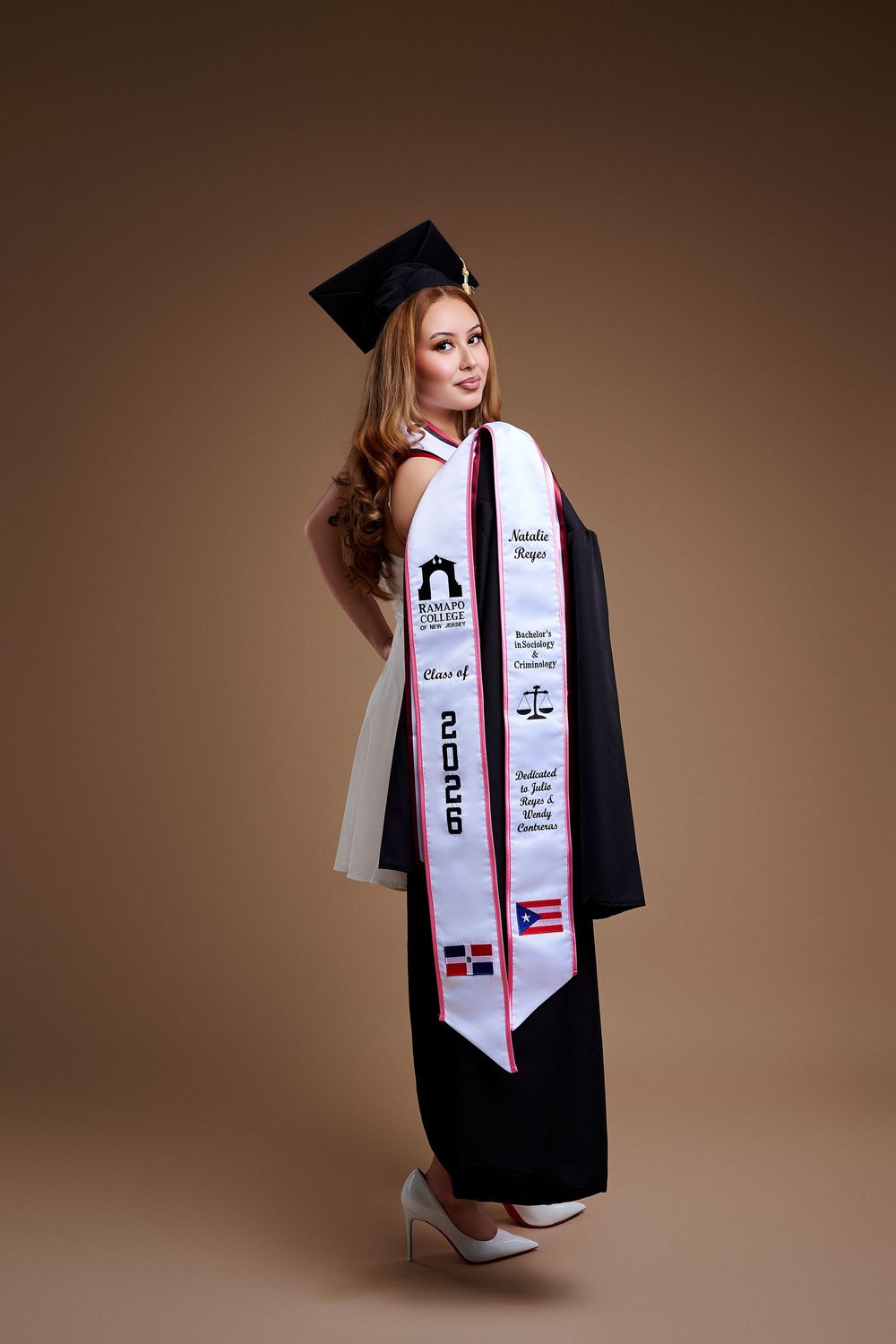 Studio graduation portrait of an RCNJ graduate showing her custom stole and gown over her shoulder, by a North NJ portrait photographer.