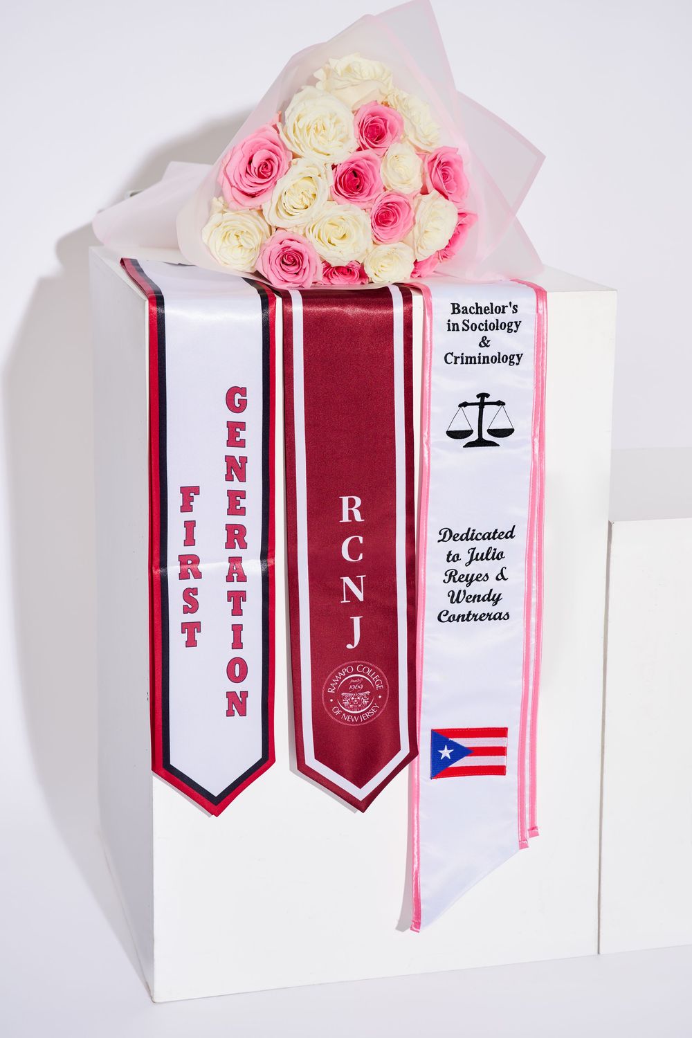 Close-up studio detail shot of custom RCNJ graduation stoles and a flower bouquet, arranged by a North NJ portrait photographer.