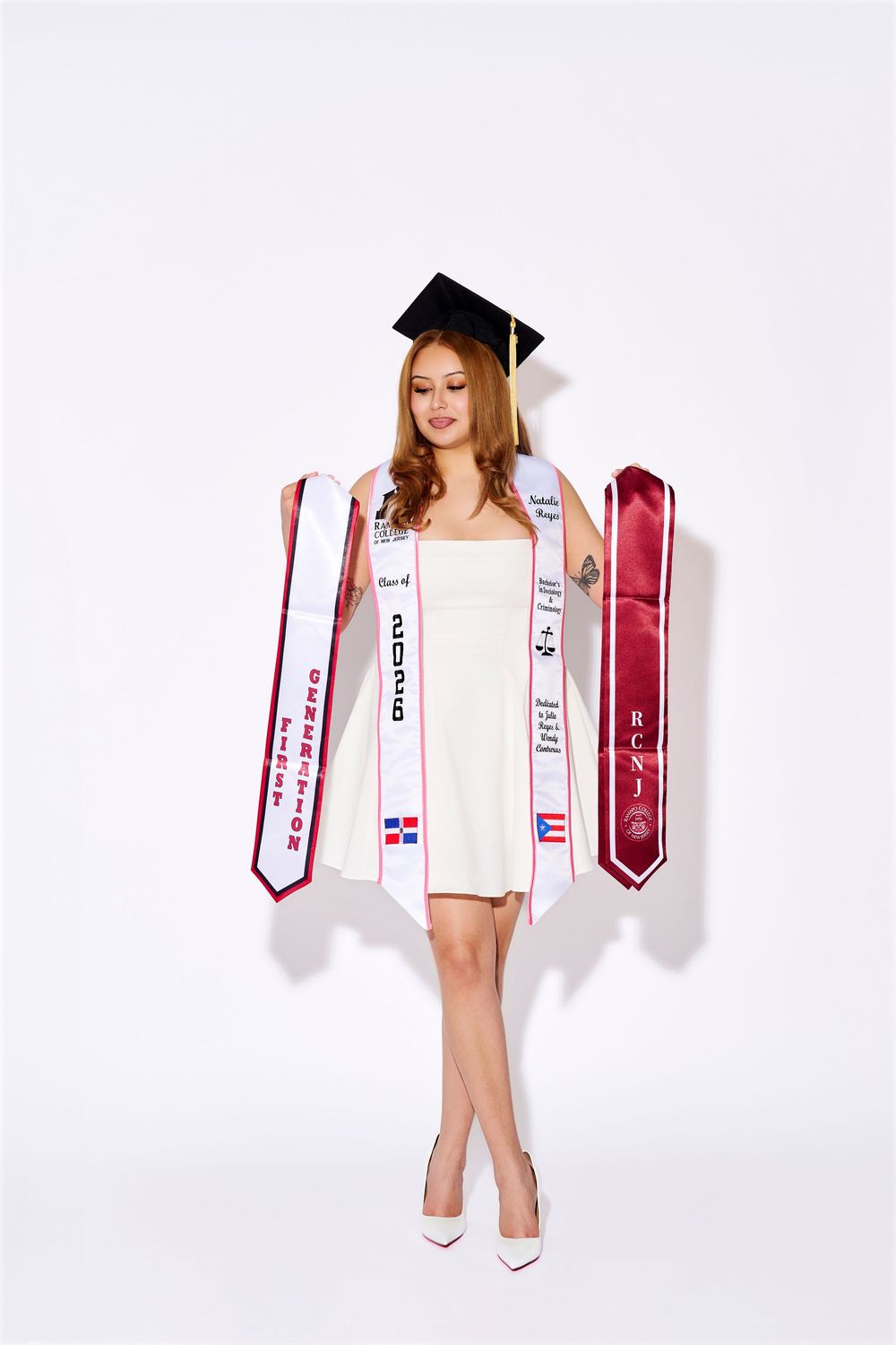 Studio graduation portrait of an RCNJ graduate holding out her academic stoles on a white backdrop, by a North NJ portrait photographer.