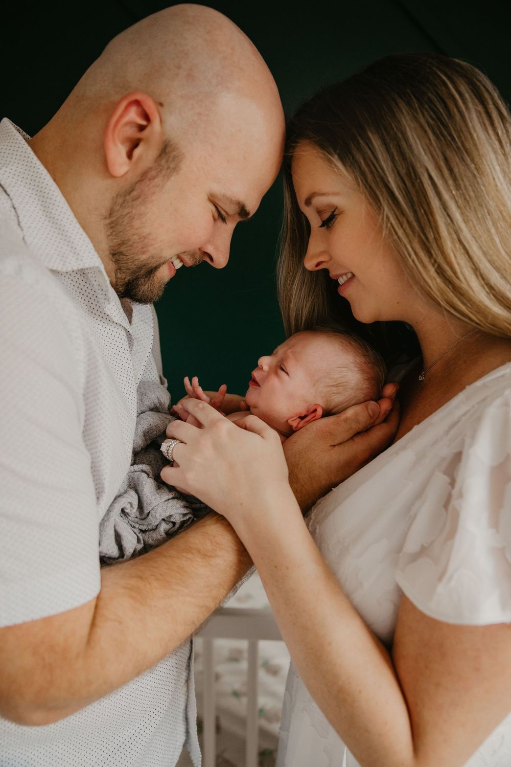 New parents tenderly hold their sleeping newborn baby together, sharing an intimate moment in a softly lit nursery.