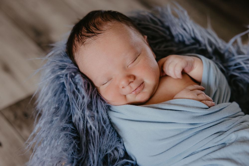 Peaceful newborn baby sleeping wrapped in a soft blue swaddle on a fluffy gray blanket in a cozy basket.