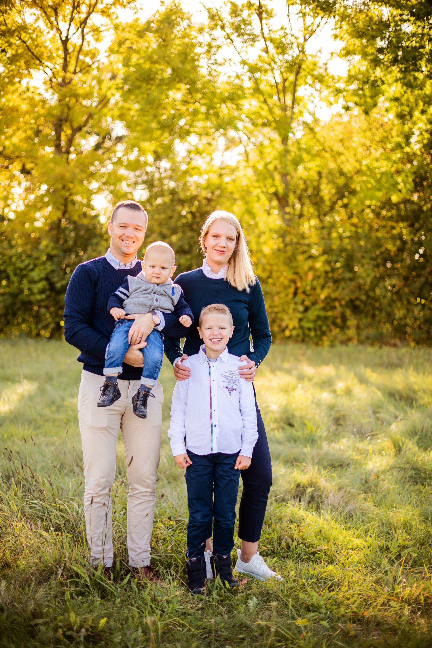 Family enjoying a sunny afternoon together in a grassy meadow surrounded by trees.