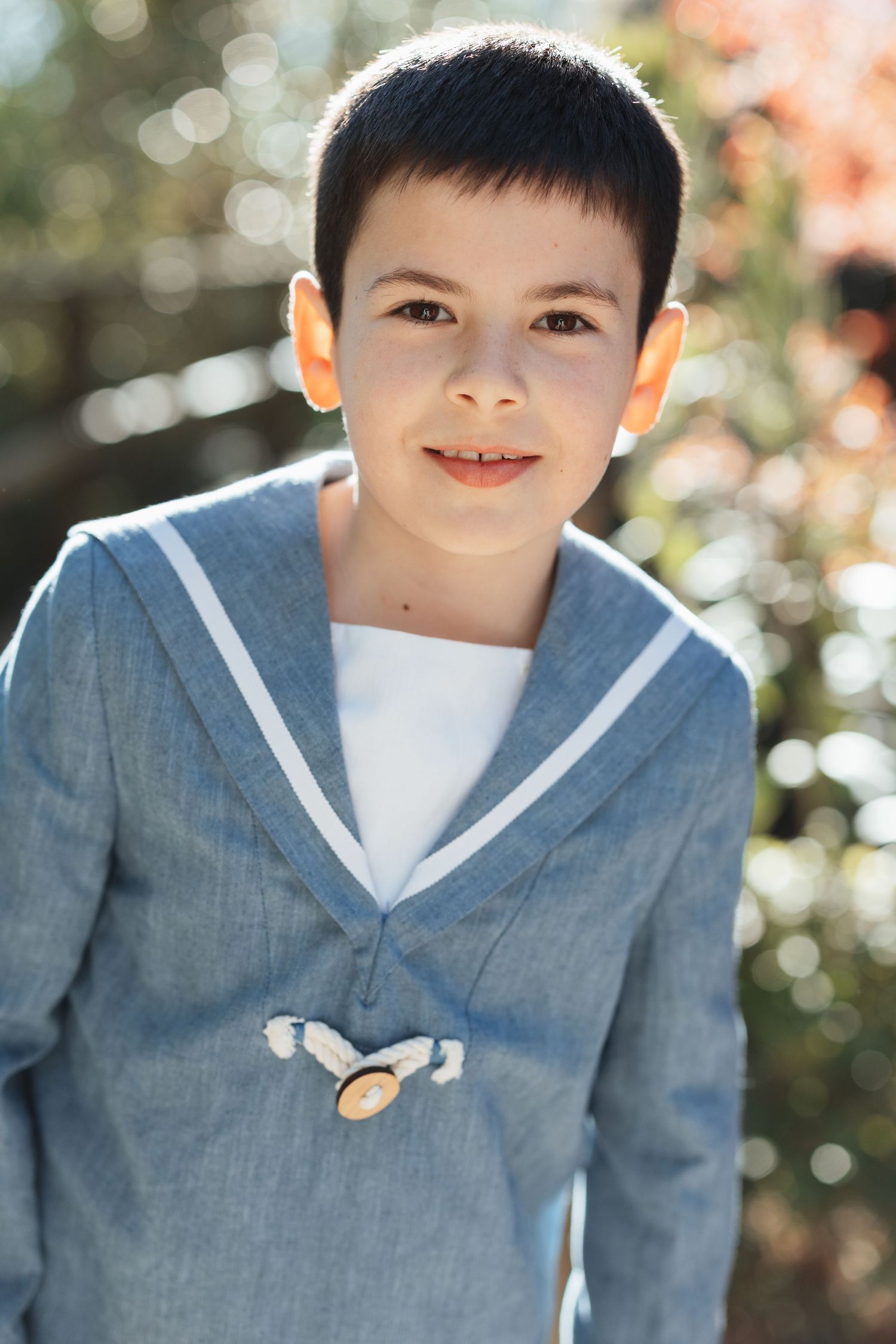 Smiling boy in a blue sailor suit posing outdoors in natural sunlight.