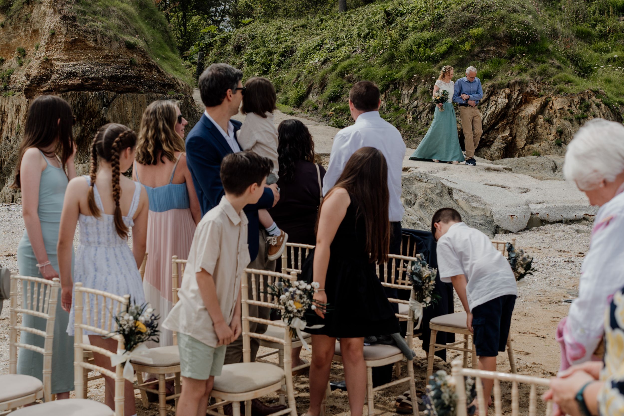 Guests watching an outdoor beach wedding ceremony with bamboo chairs and floral decorations.