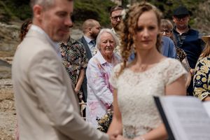 Bride and groom exchange vows at outdoor beach wedding ceremony with smiling guests watching in background.