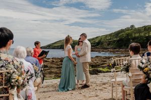 Couple exchanges vows at a scenic coastal beach wedding ceremony with officiant and guests.