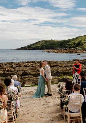 Couple exchanges vows at an intimate outdoor beach wedding ceremony with guests seated on sandy shore.