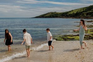 Four children playing barefoot in the gentle waves on a scenic coastal beach.