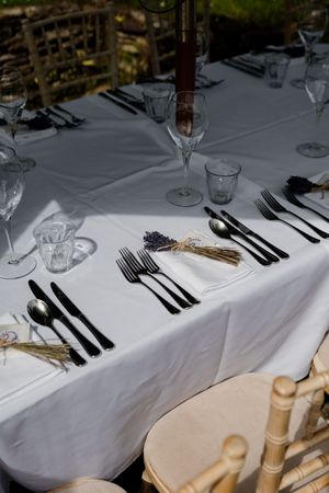 Elegant wedding table setting with black cutlery, crystal glasses, and dried lavender bouquets on white linen.