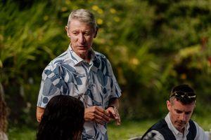 Man in floral shirt standing outdoors in a garden setting engaged in conversation.