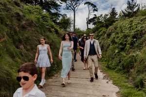 Wedding guests walking down a wooden path surrounded by lush greenery toward a beach ceremony.