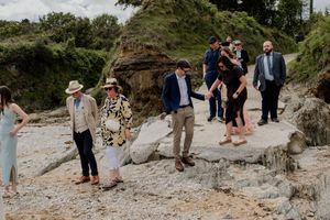 Wedding guests navigate rocky beach terrain during outdoor coastal wedding celebration.