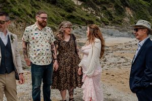 Wedding guests in casual attire socializing on a rocky beach with cliffs in the background.