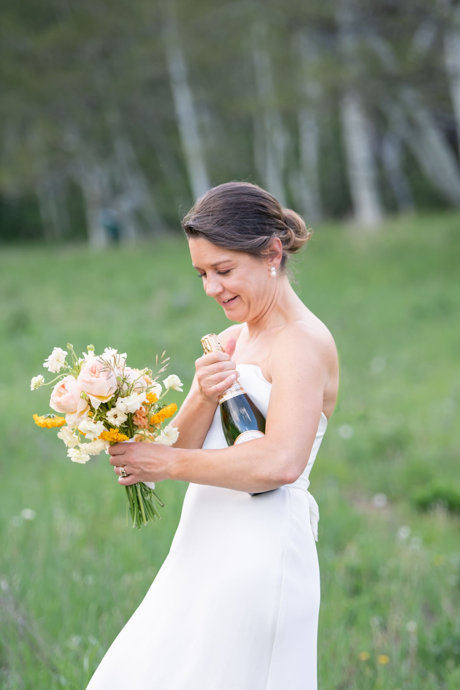 Chic candid moment of bride walking through a wildflower field with flowers and champagne for their Beaver Creek Colorado wedding