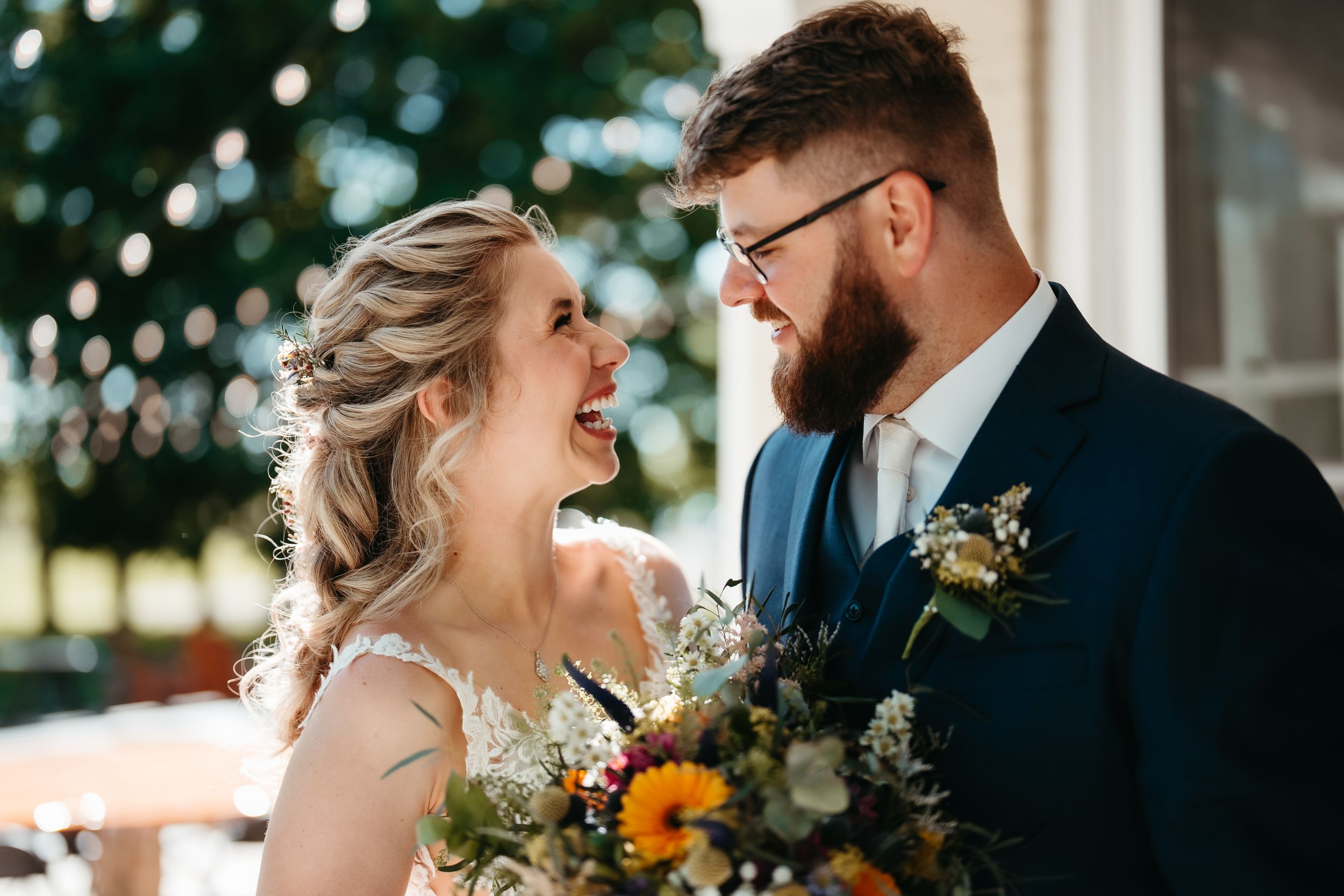 Joyful bride and groom laughing together, bride holding colorful bouquet with sunflowers on their wedding day.